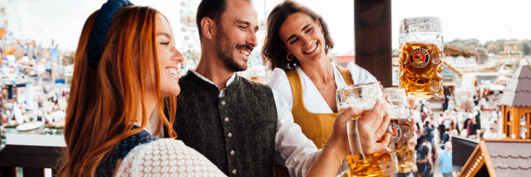 Gäste trinken PAULANER Oktoberfestbier auf dem Balkon des Festzeltes.